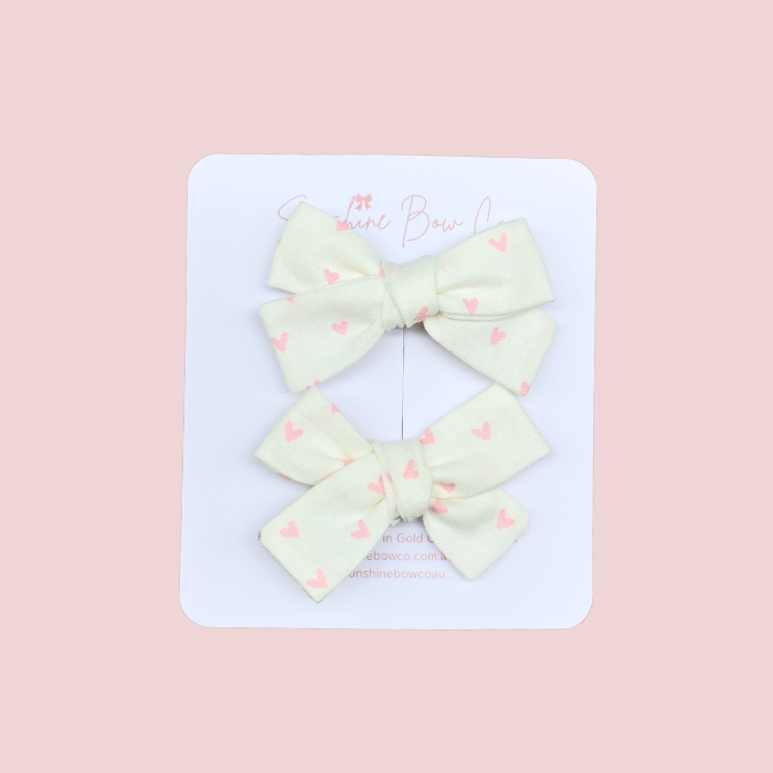 Kids pigtail hair bow set in white with pink hearts, charming and perfect for adding a sweet touch to hairstyles.