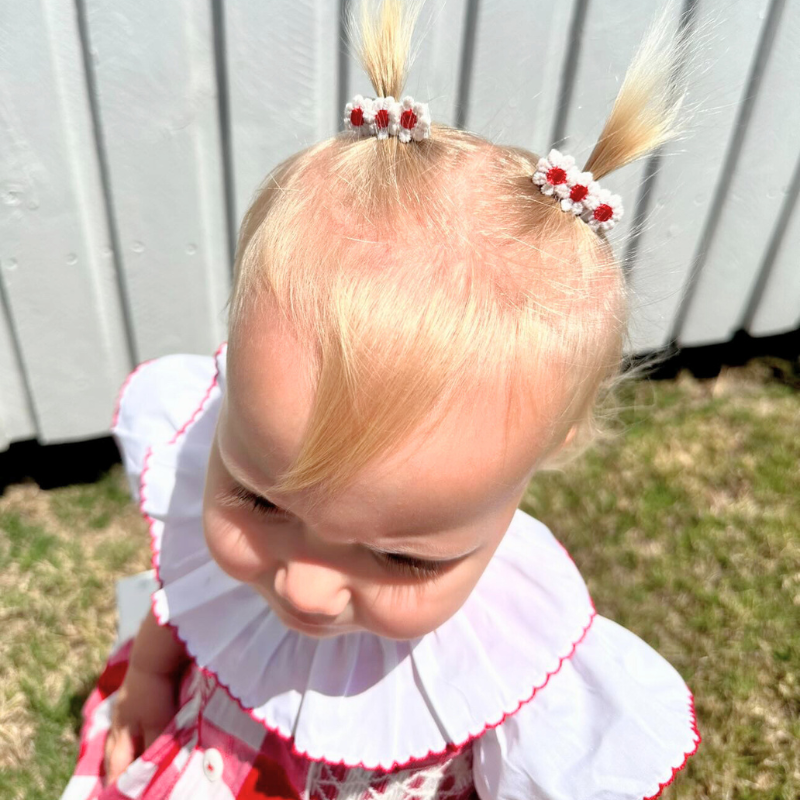 Toddler wearing the Red Daisies Clip Set, featuring two delicate red daisy designs. Each clip measures about 3.5 cm, adding a charming pop of color to her hairstyle. Ideal for everyday wear or special occasions, these clips offer a sweet and playful accent to any outfit.